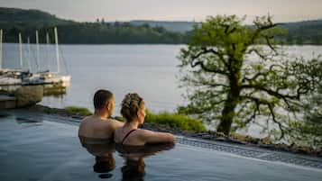 A couple in a private infinity pool overlooking a lake with boats and greenery in the background.