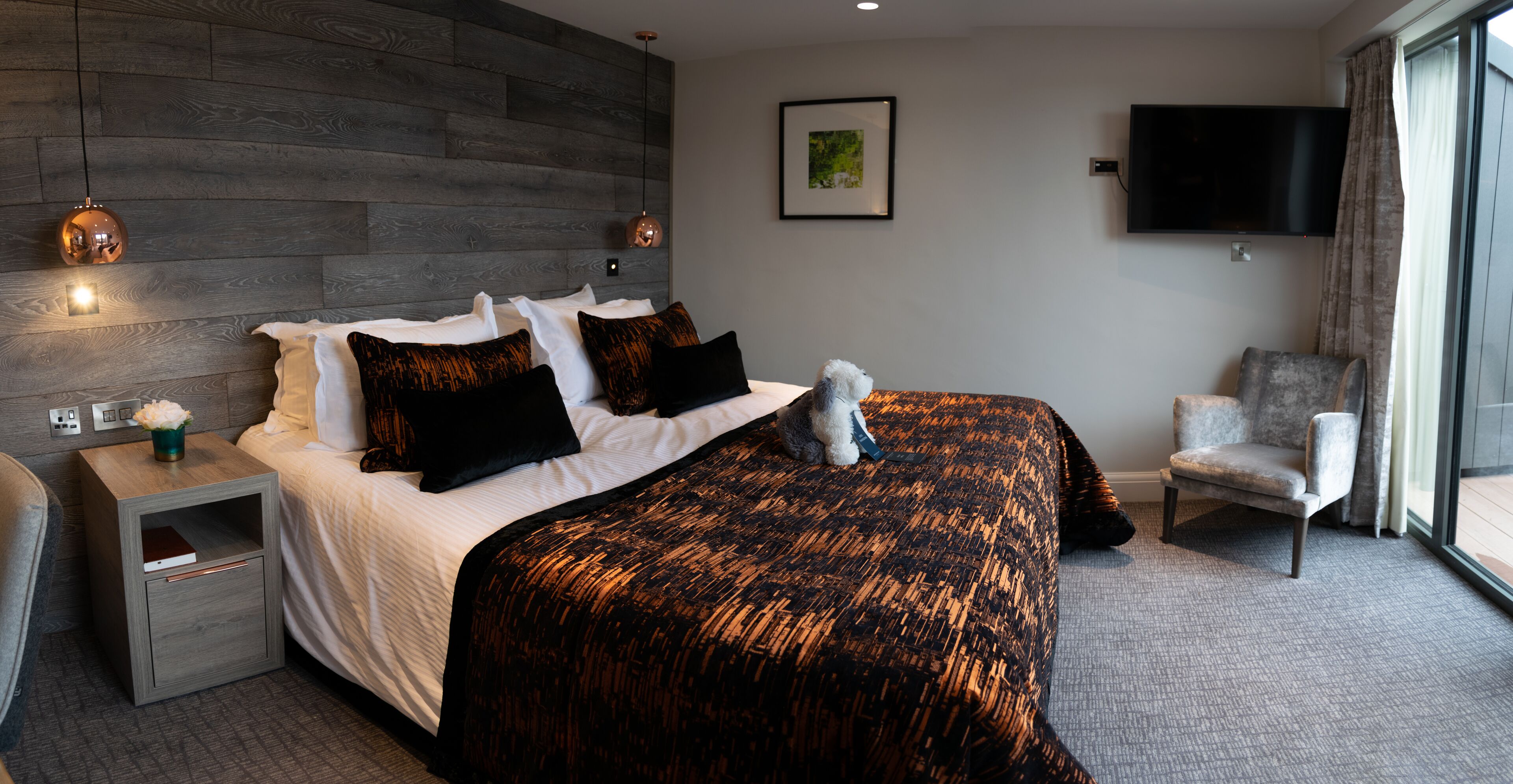 A modern hotel room with a large bed, a nightstand, a chair, a TV, and a window with curtains.