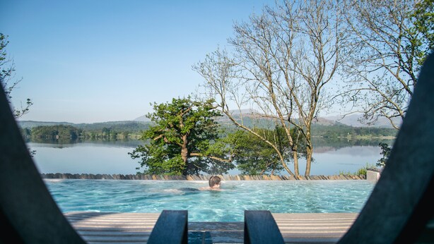 A pool with a view of a lake and mountains, surrounded by trees and wooden deck chairs. - Low Wood Bay Resort & Spa (Windermere)