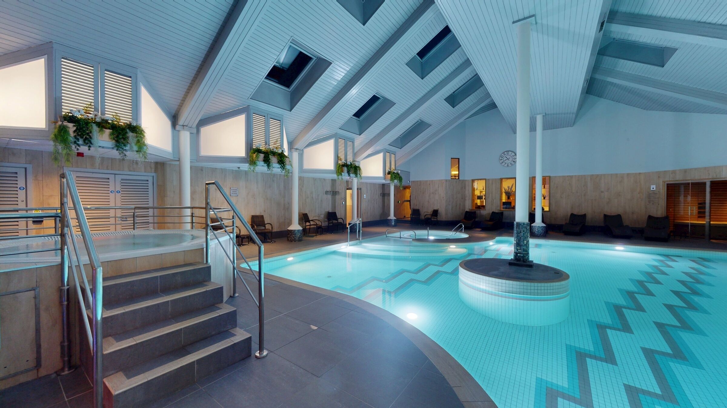A swimming pool with a zigzag tile pattern, a staircase with metal railings, and a ceiling with skylights.