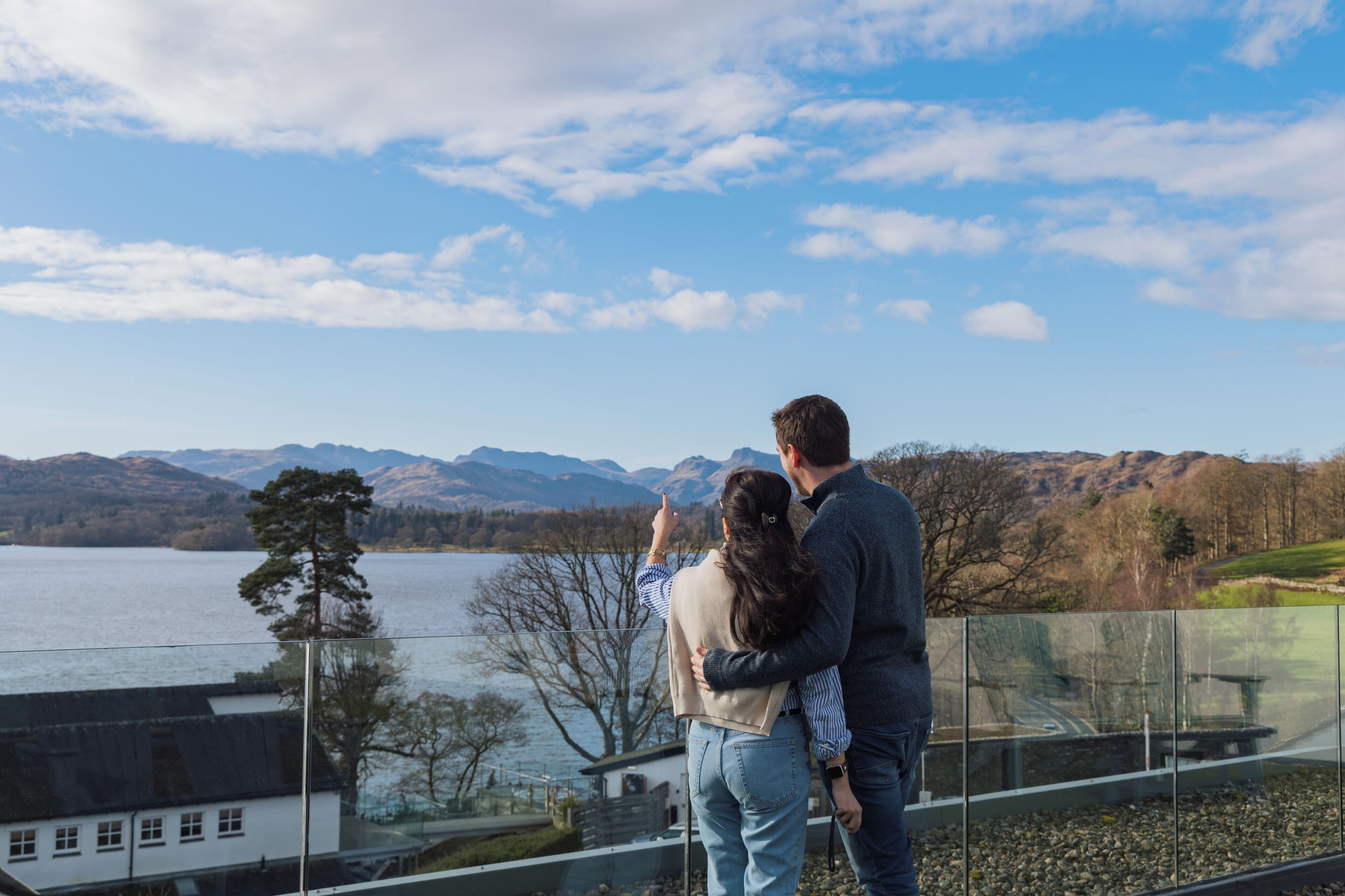 Et par der står på en balkon med udsigt over en sø og fjerne bjerge.