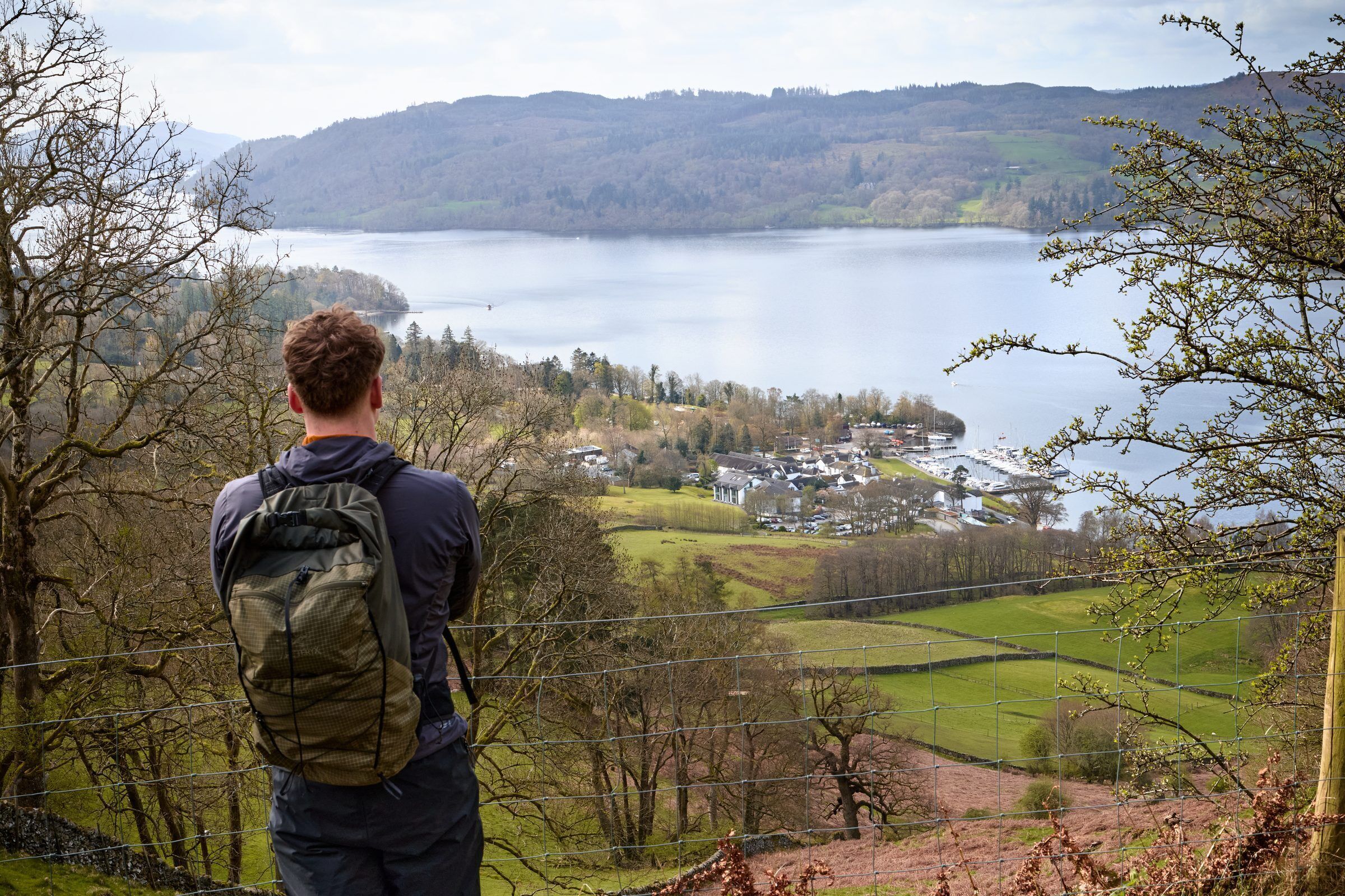 A person standing at a high vantage point overlooking a lake with a village in the distance.