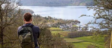 A person standing at a high vantage point overlooking a lake with a village in the distance.