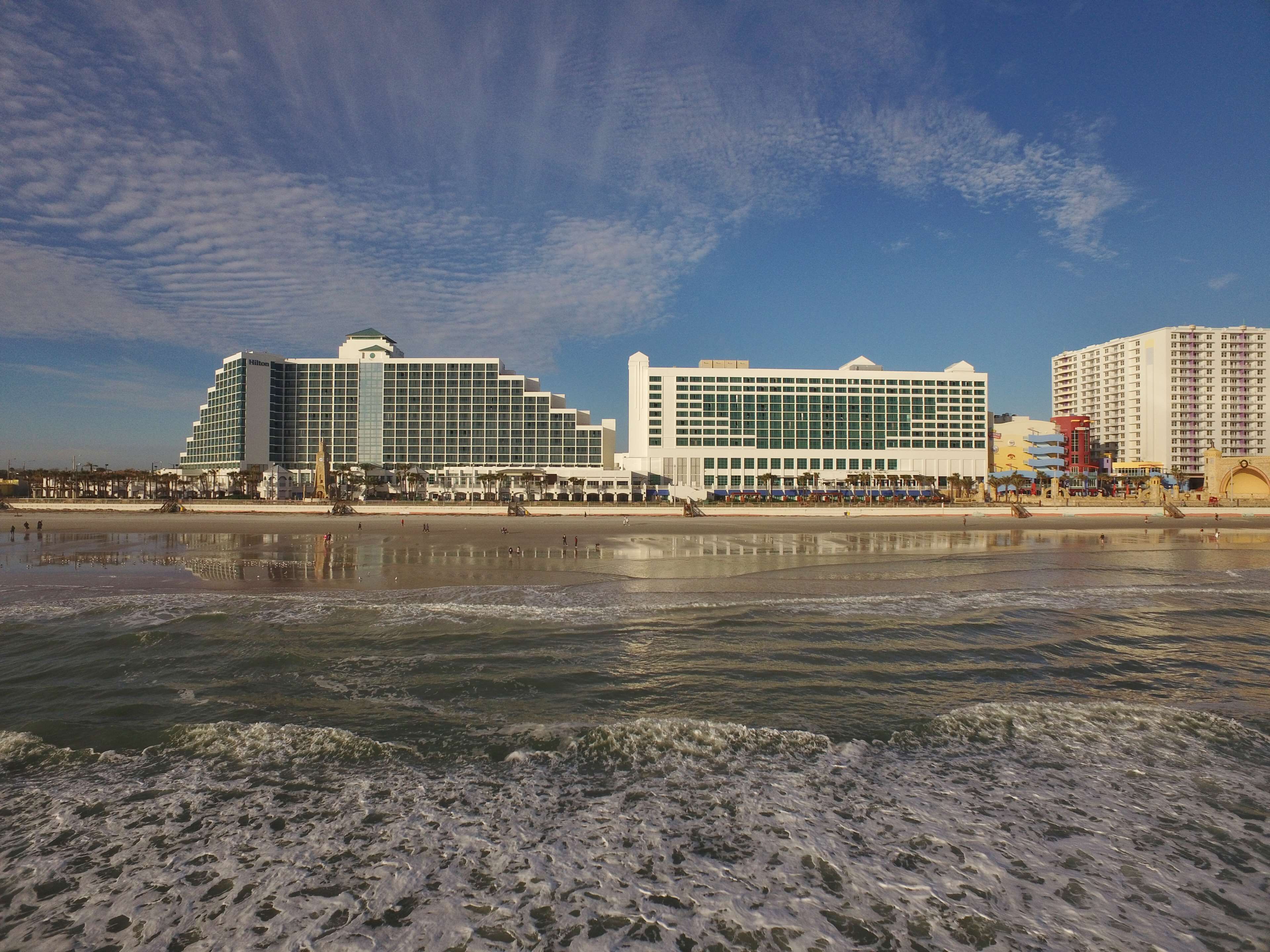 A beachfront hotel with a large building, a pool, and a beach in the foreground.
