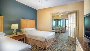 A hotel room with two beds, a desk with a lamp, a television, and a view of the outdoor patio area.
