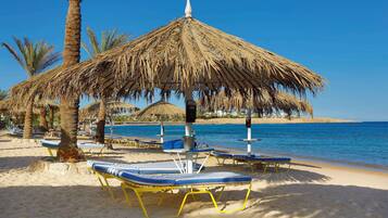 A beach with sun loungers and a thatched umbrella.