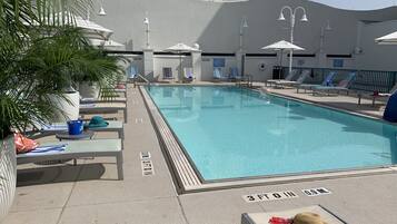 A swimming pool with lounge chairs and umbrellas, surrounded by a building with balconies.