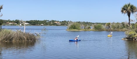 Un lago tranquilo con kayaks y una casa al fondo.