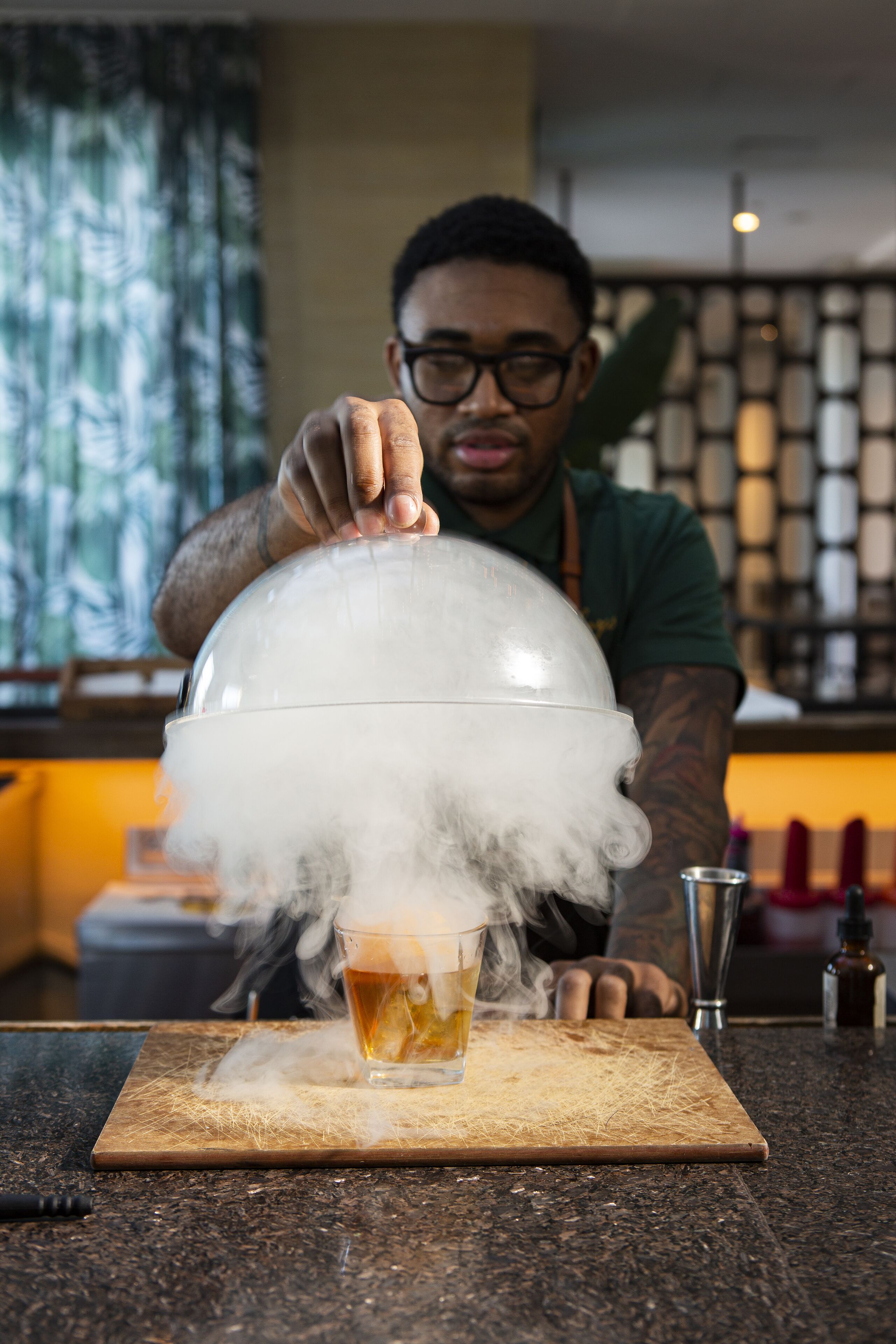 A person pouring a drink from a dome-shaped container onto a wooden board.