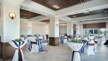 A spacious indoor area with multiple tables and chairs, wooden ceiling panels, and wall-mounted lighting fixtures.