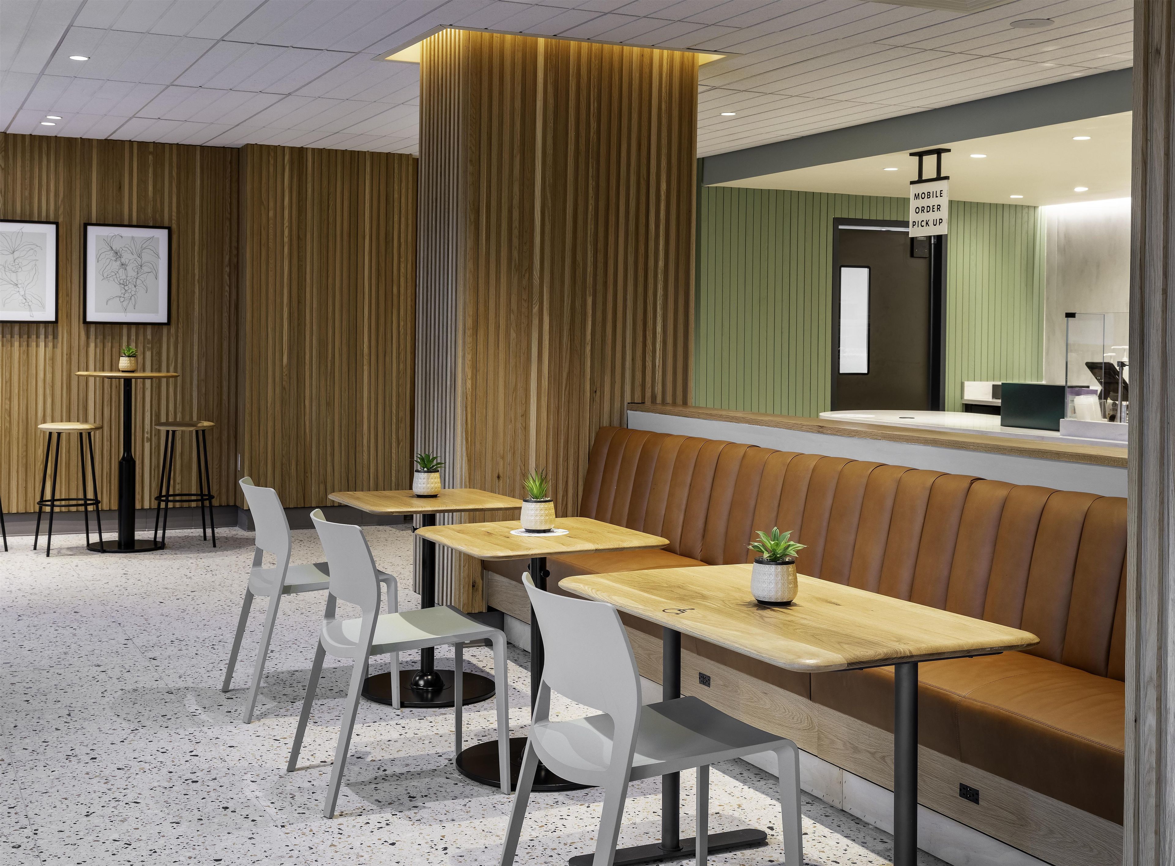 A modern interior with wooden panel walls, a seating area with tables and chairs, and a counter with a sign indicating mobile order pickup.
