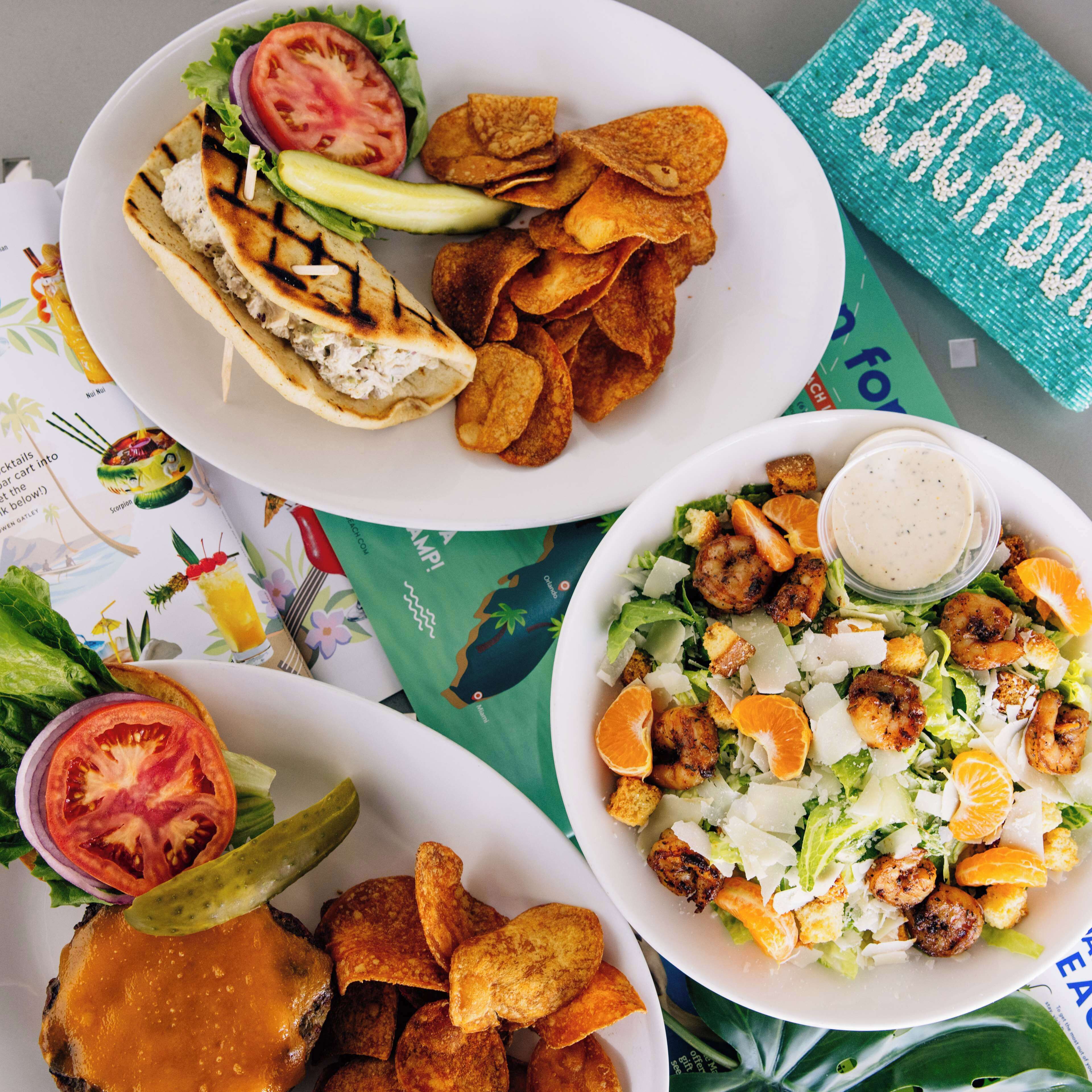 A table with three plates of food, including a salad, grilled chicken sandwich, and a burger with fries.