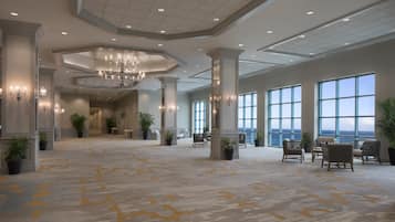 A spacious lobby with a high ceiling, chandeliers, large windows, and a patterned carpet.