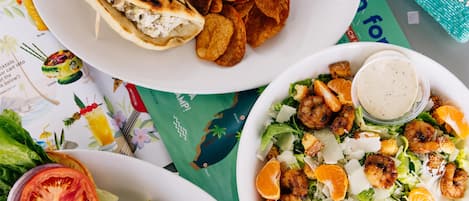 Variedad de alimentos, incluyendo una ensalada con aderezo, pollo a la parrilla y un sándwich con papas fritas.