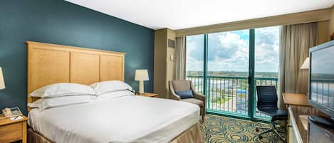 Quarto de hotel com cama grande, escrivaninha, cadeira, televisão e varanda com vista.