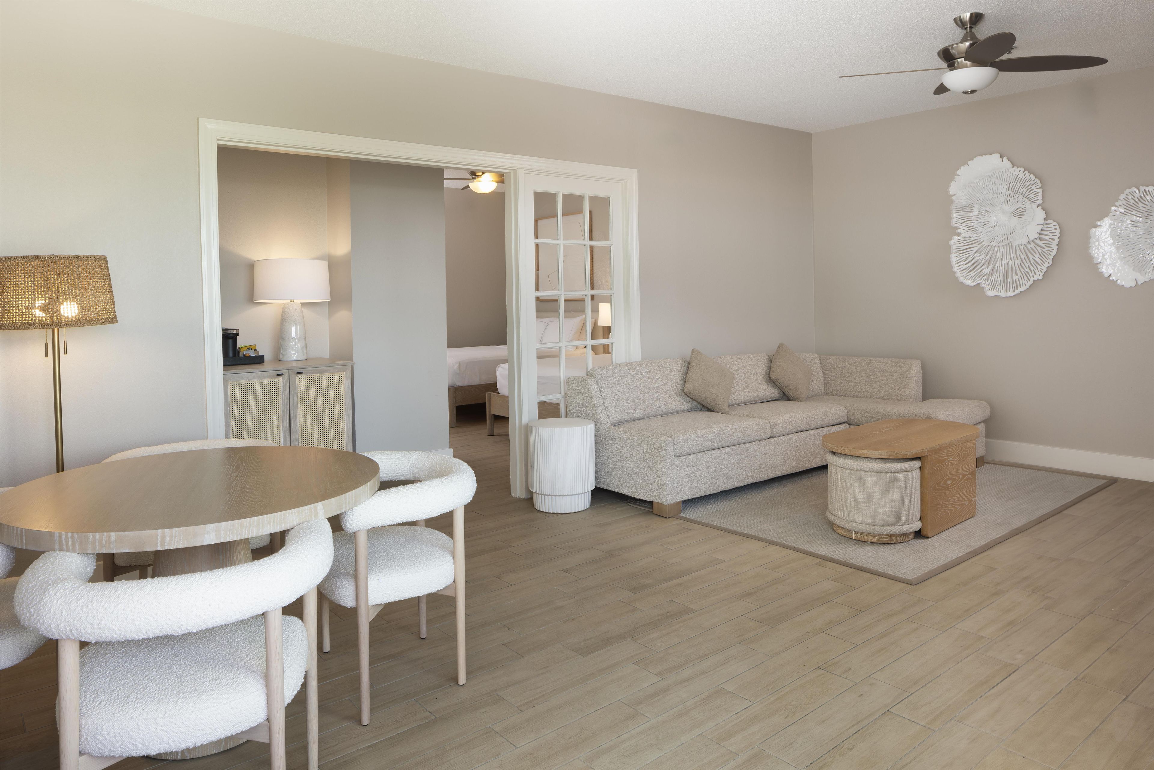 A modern living room with a round table, white cushioned chairs, a sofa, and a coffee table.