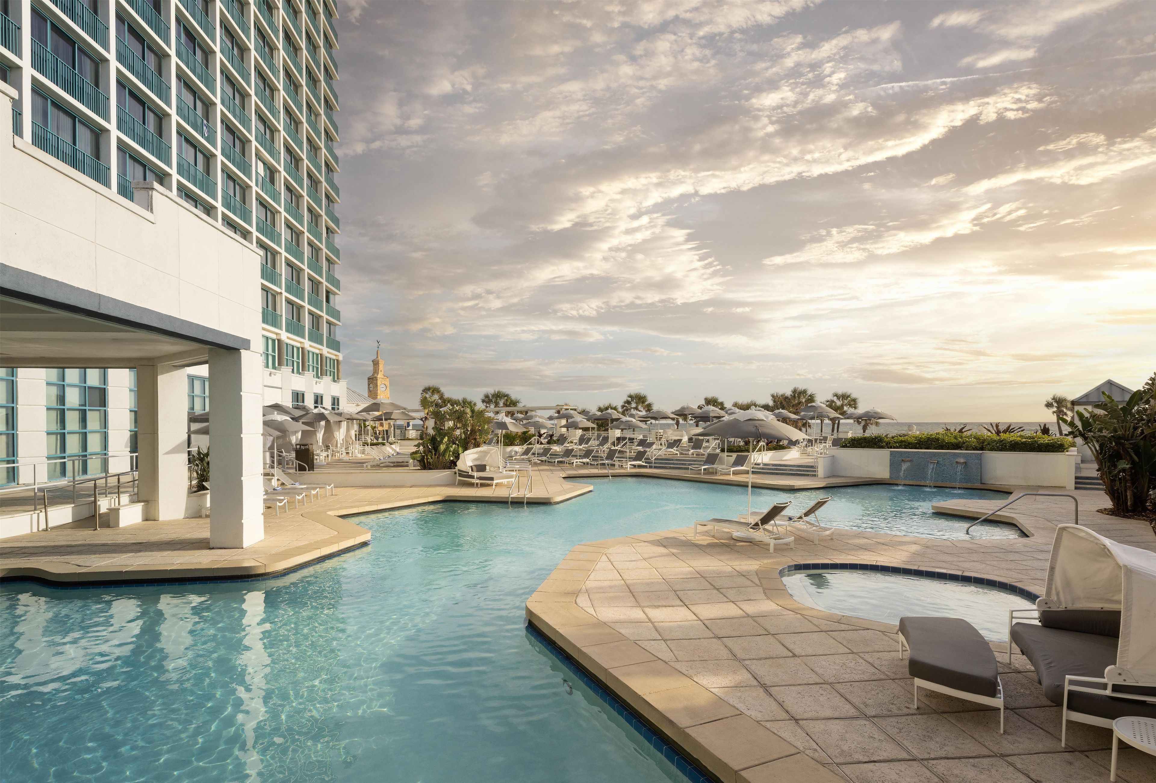 A hotel pool area with multiple swimming pools, lounge chairs, and umbrellas.