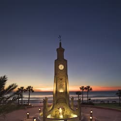 Stunning clock tower stands tall amidst lush palm trees and ocean views.