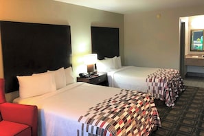 A hotel room with two beds, a desk, a chair, and a bathroom visible through the door.