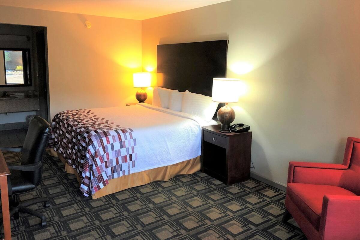 A hotel room with a bed, two bedside lamps, a chair, a desk, and a television.