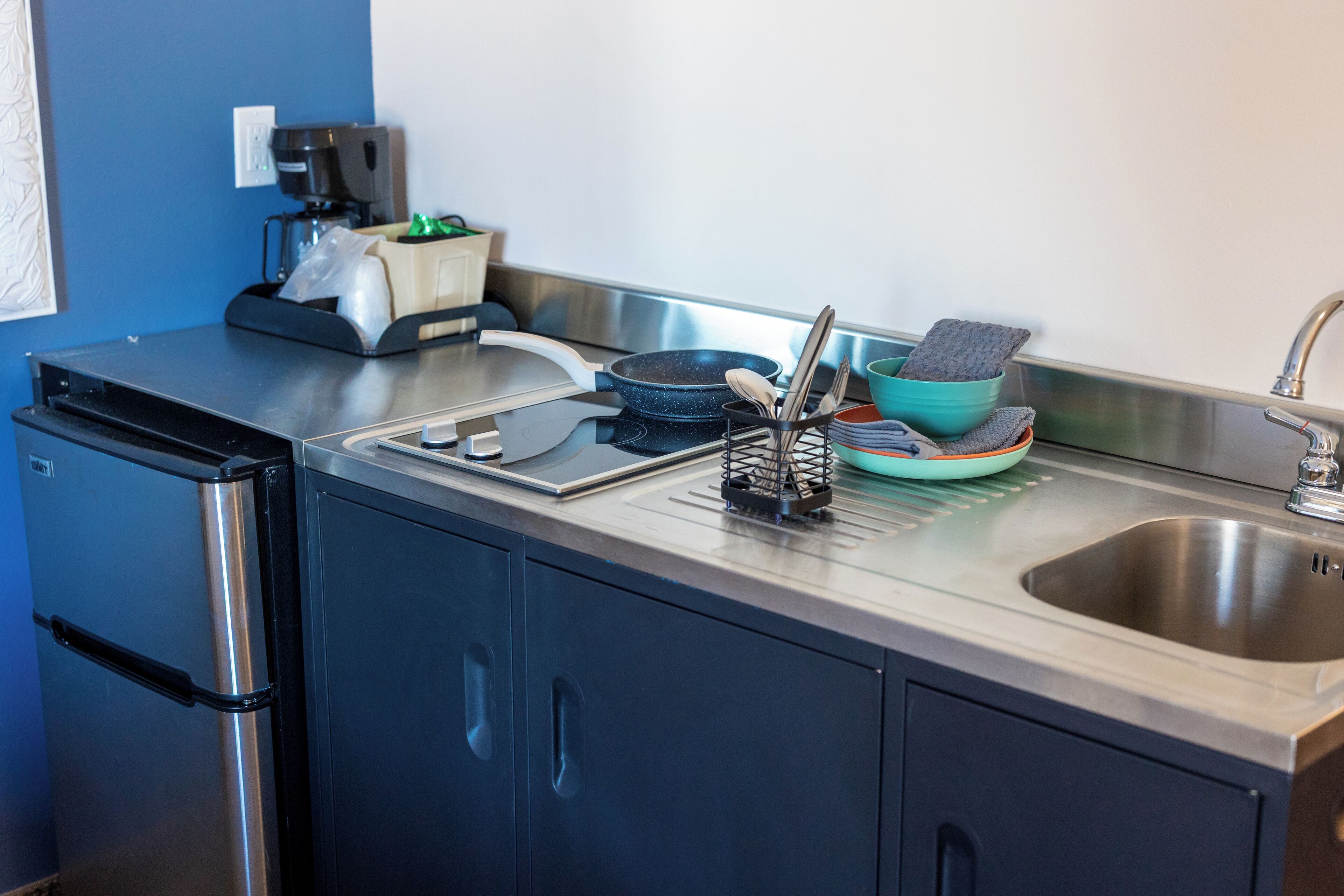 A compact kitchen with a stainless steel refrigerator, a coffee maker, a toaster, and a sink.