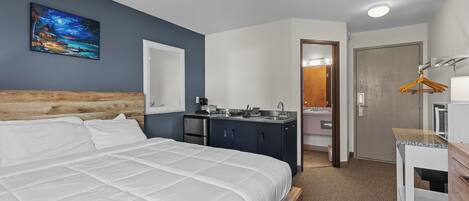 Habitación de hotel con una cama grande, una kitchenette pequeña, un baño con espejo y un cabecero de madera.