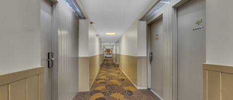 A hotel hallway with patterned carpet, doors on both sides, and a 'No Smoking' sign on one door.