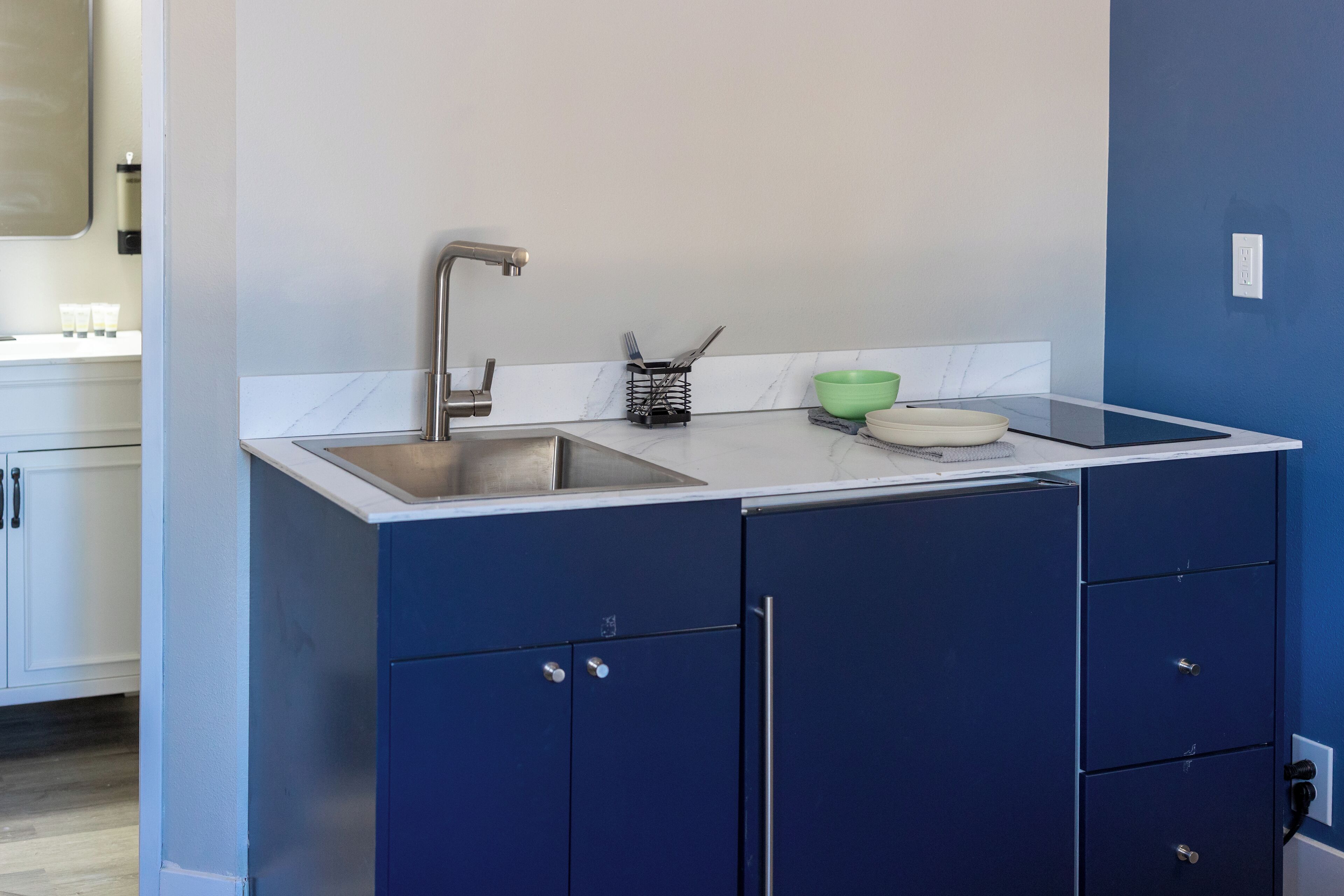 A modern kitchen with a stainless steel sink, a green bowl, and a tablet on the counter.