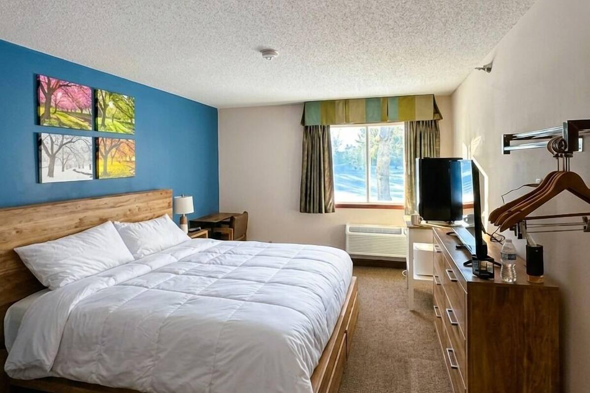 A hotel room with a large bed, a TV, a desk with a computer, and a window with curtains.