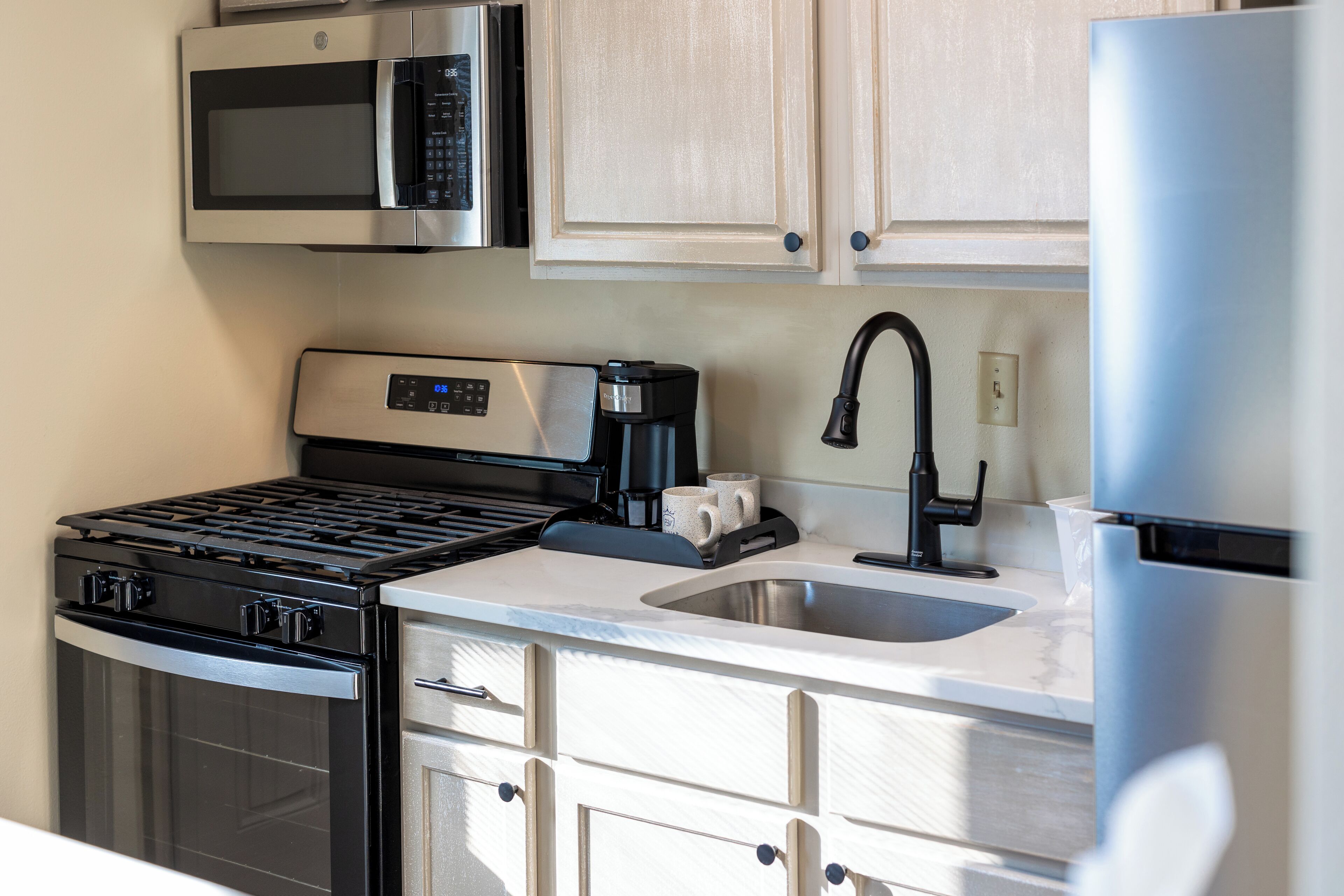 Una cocina moderna con electrodomésticos de acero inoxidable, microondas integrado, cafetera y pileta.