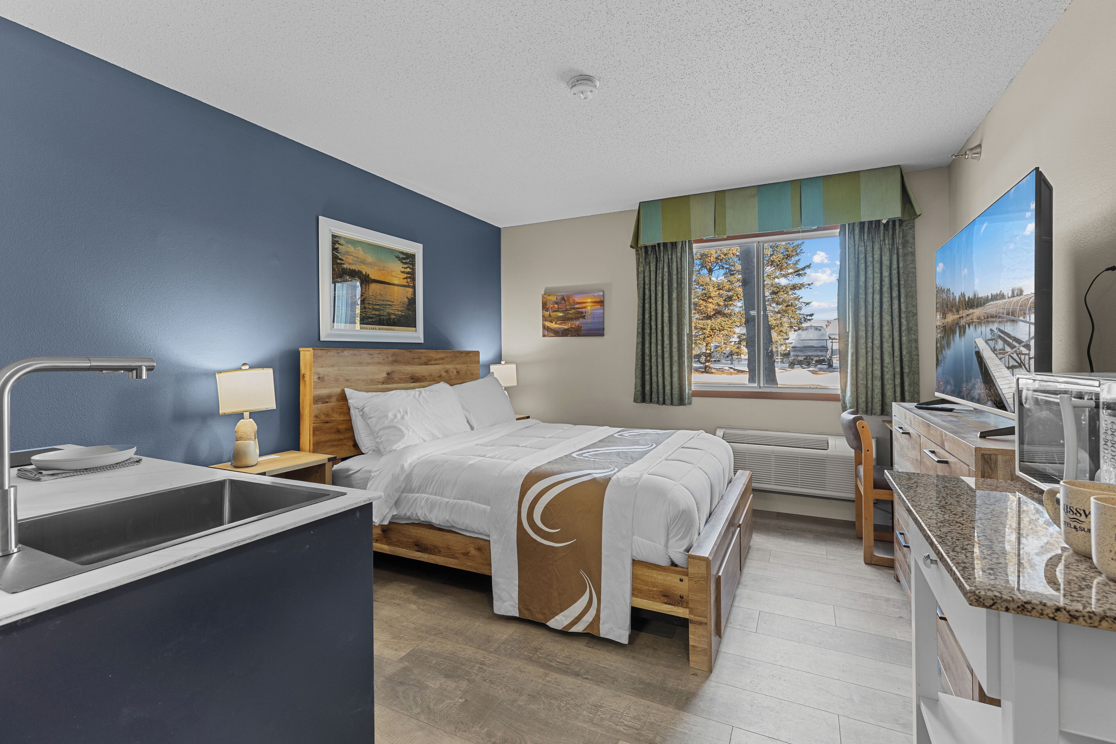 Habitación de hotel con cama, escritorio, televisor, ventana con cortinas y vista a un puente.
