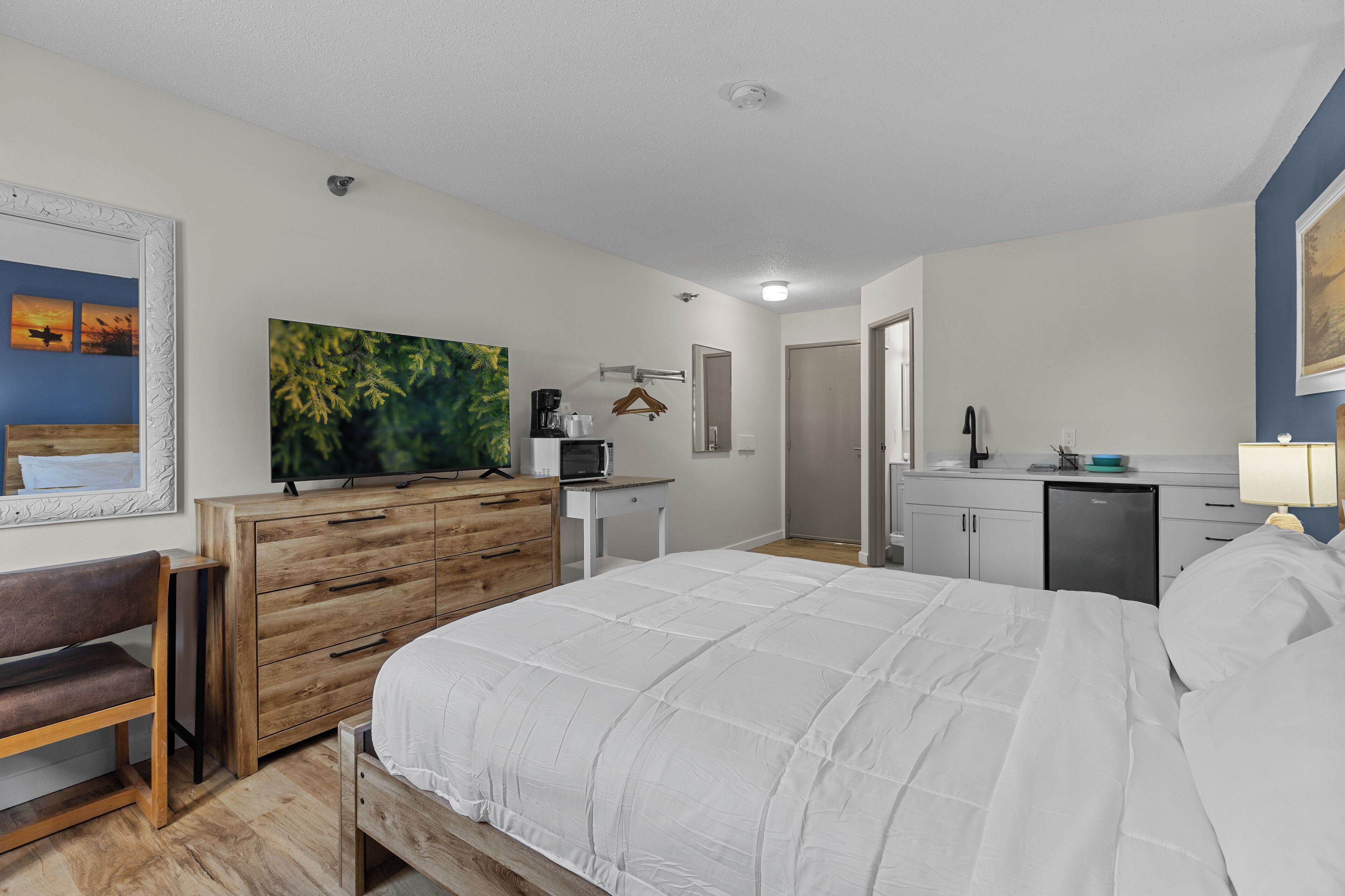 Un dormitorio con cama, cómoda de madera, televisor y una pequeña kitchenette.