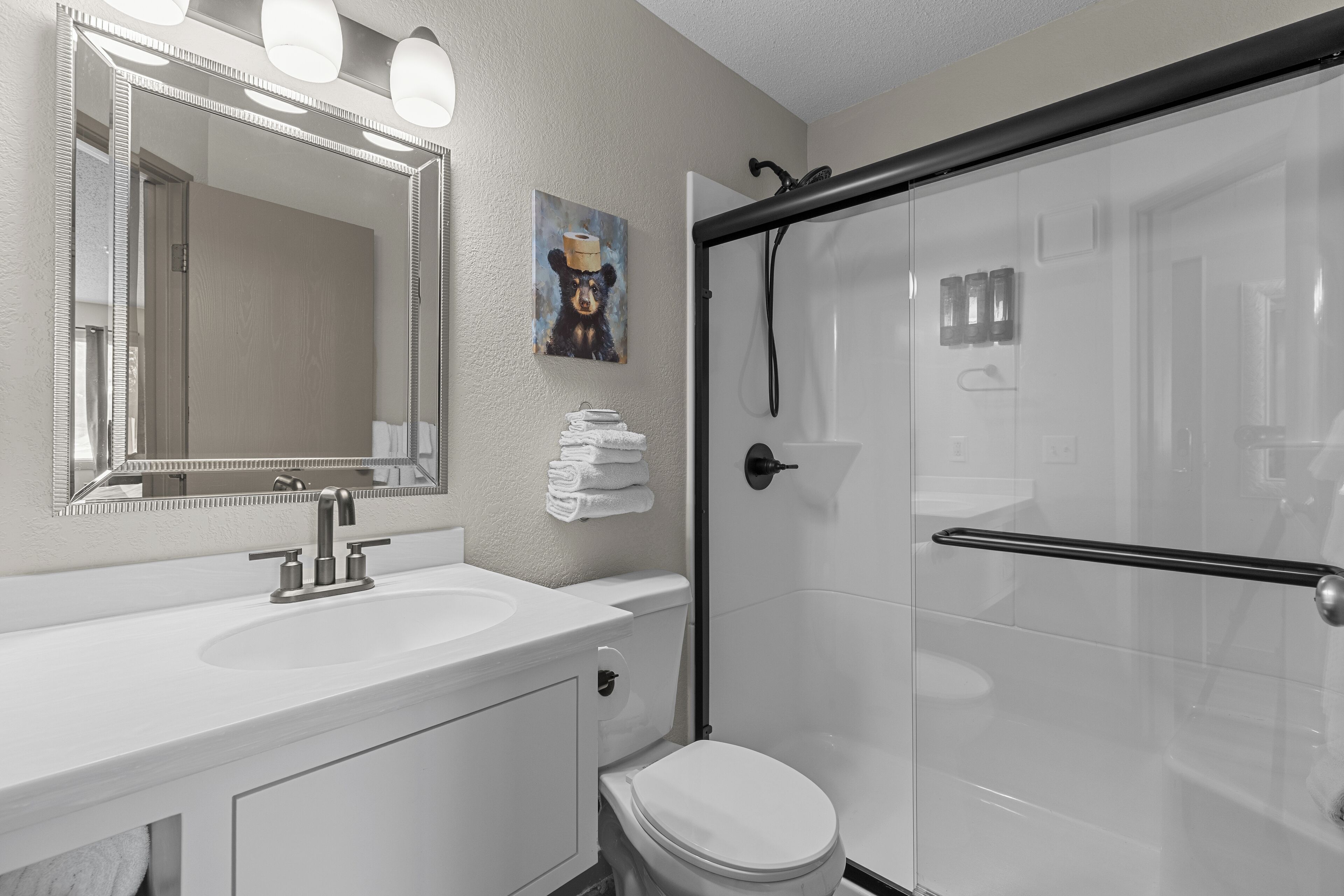 A modern bathroom with a white sink, mirror, and toilet. There is a glass shower enclosure and a towel rack with folded towels.