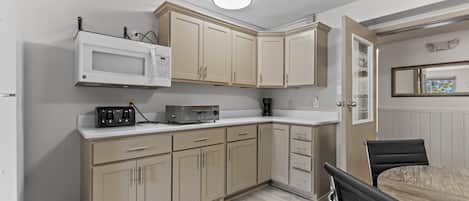 A kitchen with beige cabinets, a microwave, a coffee maker, and a dining area with a table and chairs.