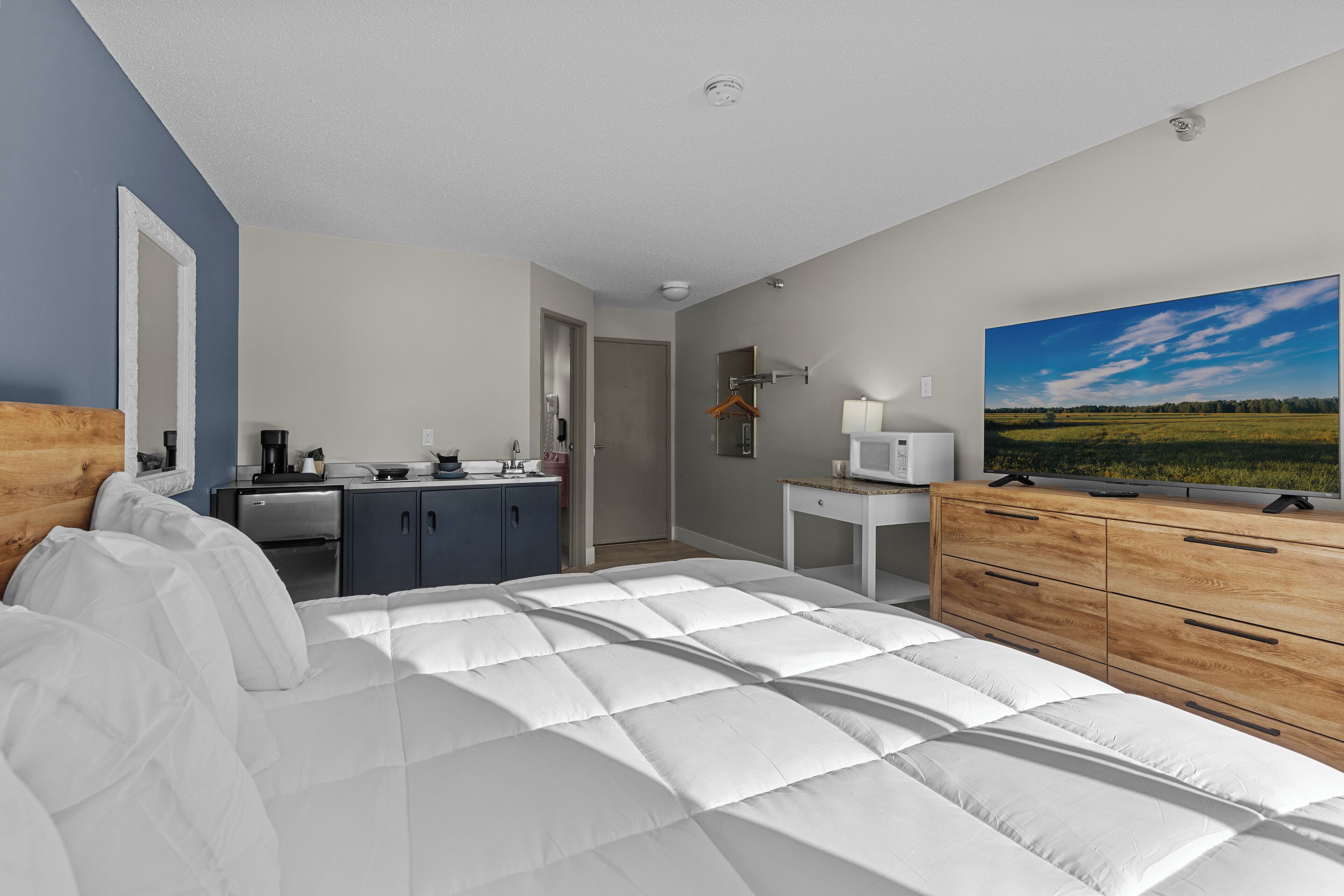 A bedroom with a bed, a dresser, a TV, a desk, and a window with a view of a field.