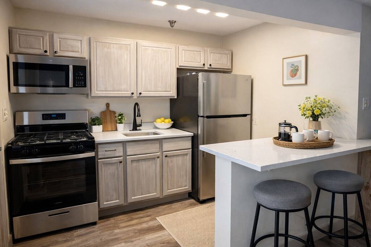 A modern kitchen with stainless steel appliances, light wood cabinets, a central island with stools, and a small decorative plant.