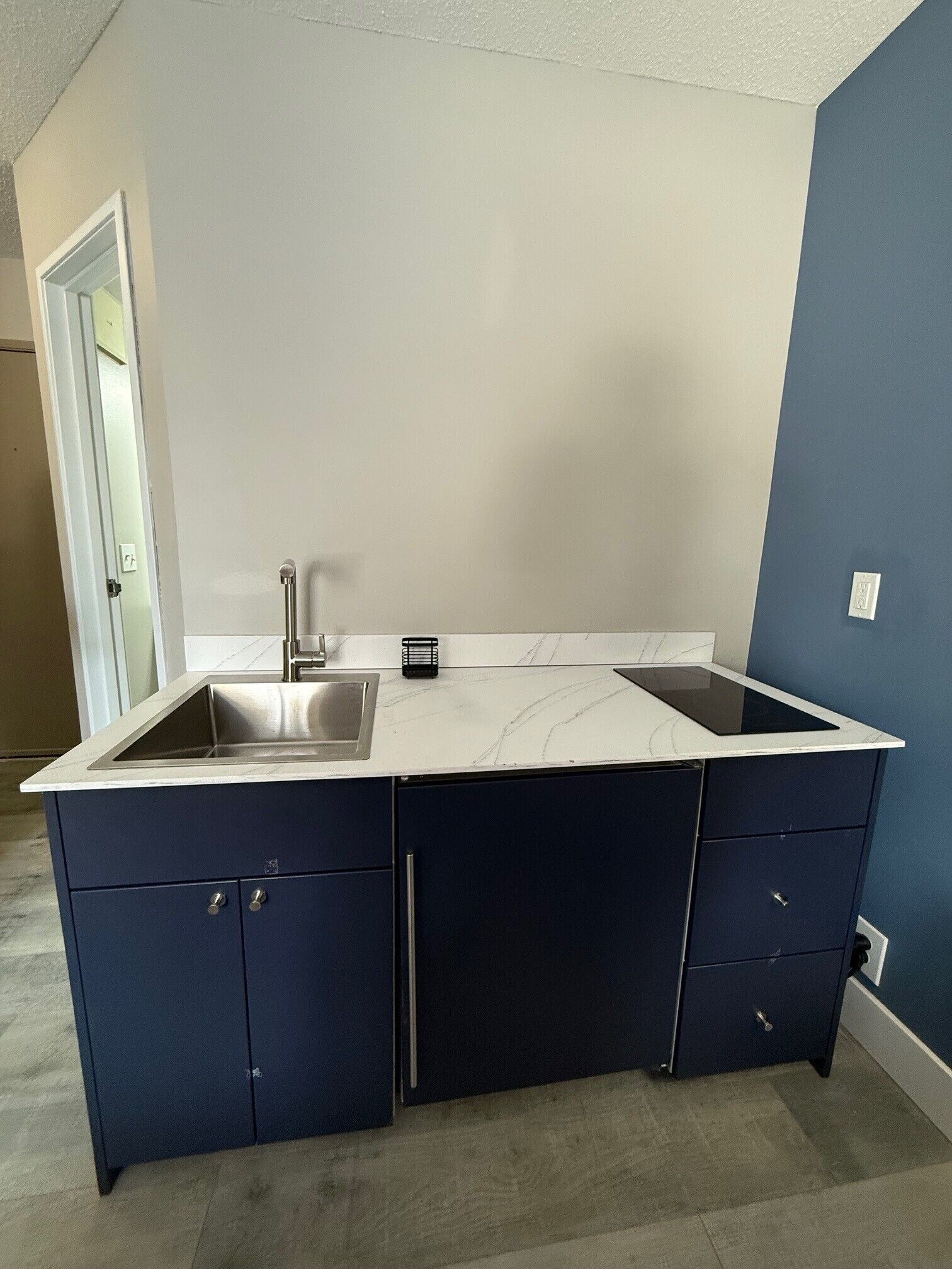 A kitchen with a white marble countertop, a stainless steel sink, and dark blue cabinets.