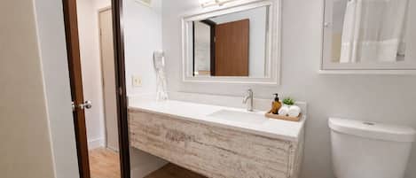 A bathroom with a white sink, a mirror, a wooden vanity, a toilet, and a shower curtain.