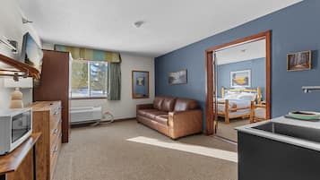 Una habitación compacta con kitchenette, un sofá de cuero marrón, una cama y una ventana con cortinas.
