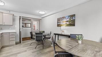 A modern kitchen with white cabinets, a dining area with a wooden table and black chairs, and a painting on the wall.