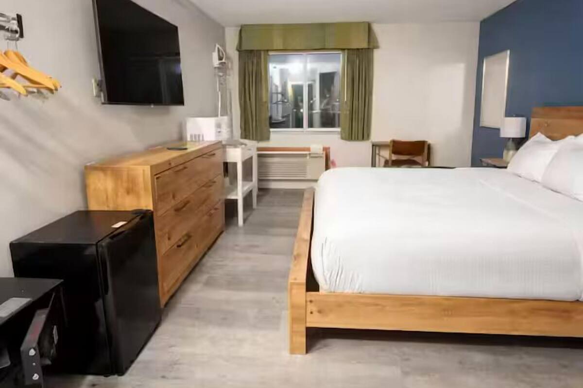 A hotel room with a wooden bed, a flat-screen TV, a wooden dresser, a desk, and a chair.