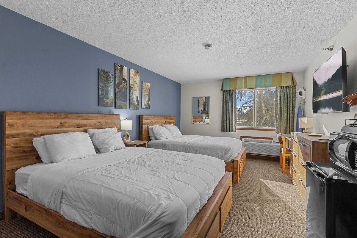 A hotel room with two beds, a TV, a desk, and a window with curtains.