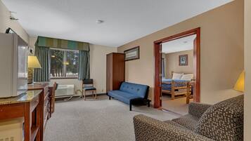 A hotel room with a bed, a sofa, a desk with a lamp, and a window with curtains.