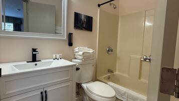 A bathroom with a white sink, mirror, and toilet. There is a shower area with a glass door and a towel rack.