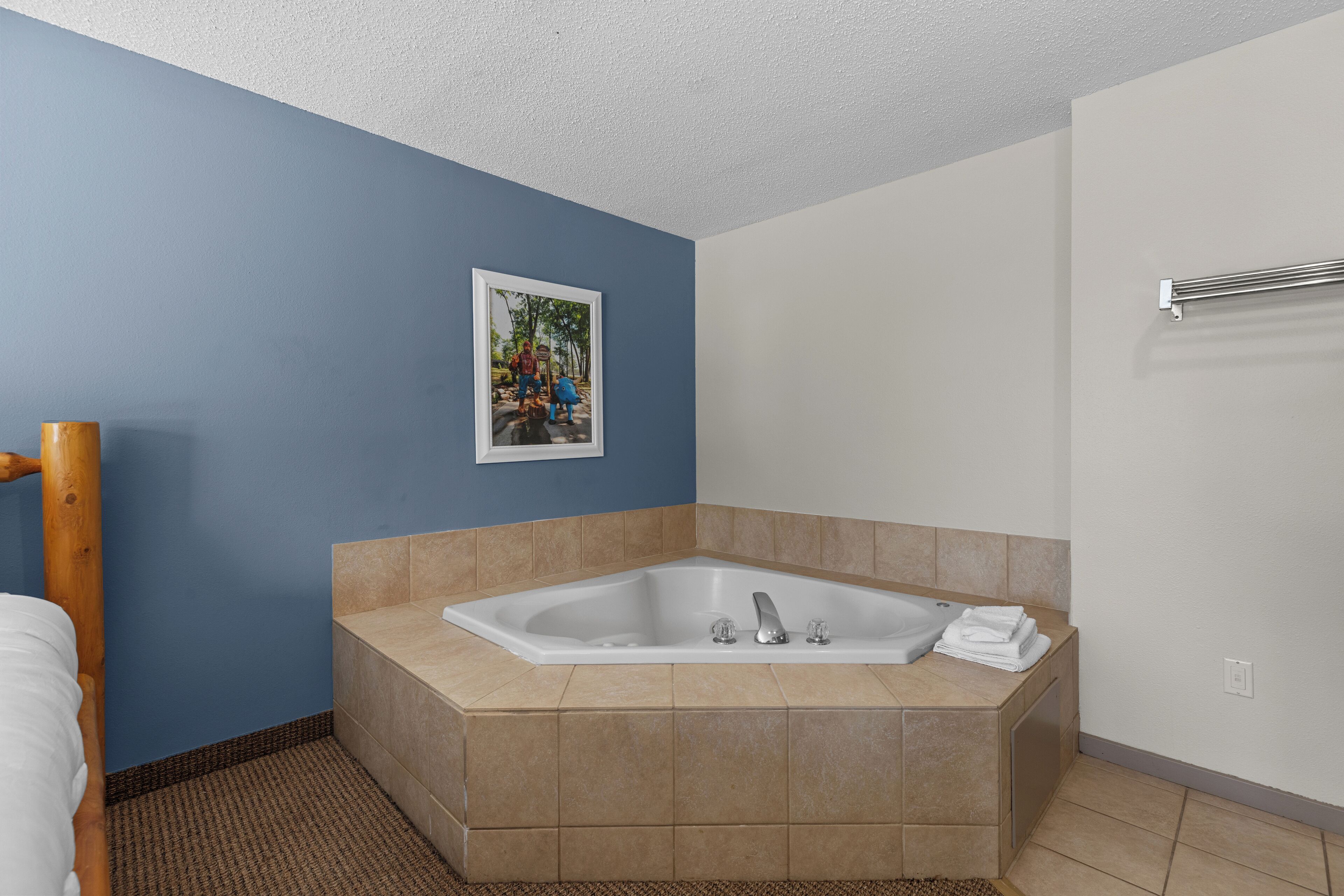 A modern bathroom with a large bathtub, a wooden bed frame, and a framed picture on the wall.