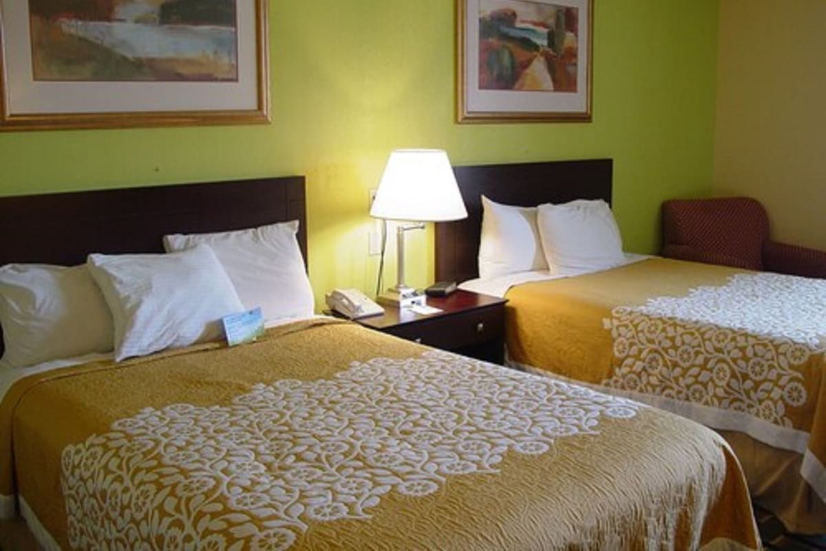 Een hotelkamer met twee bedden, een nachtkastje met een lamp, en twee ingelijste kunstwerken aan de muur.