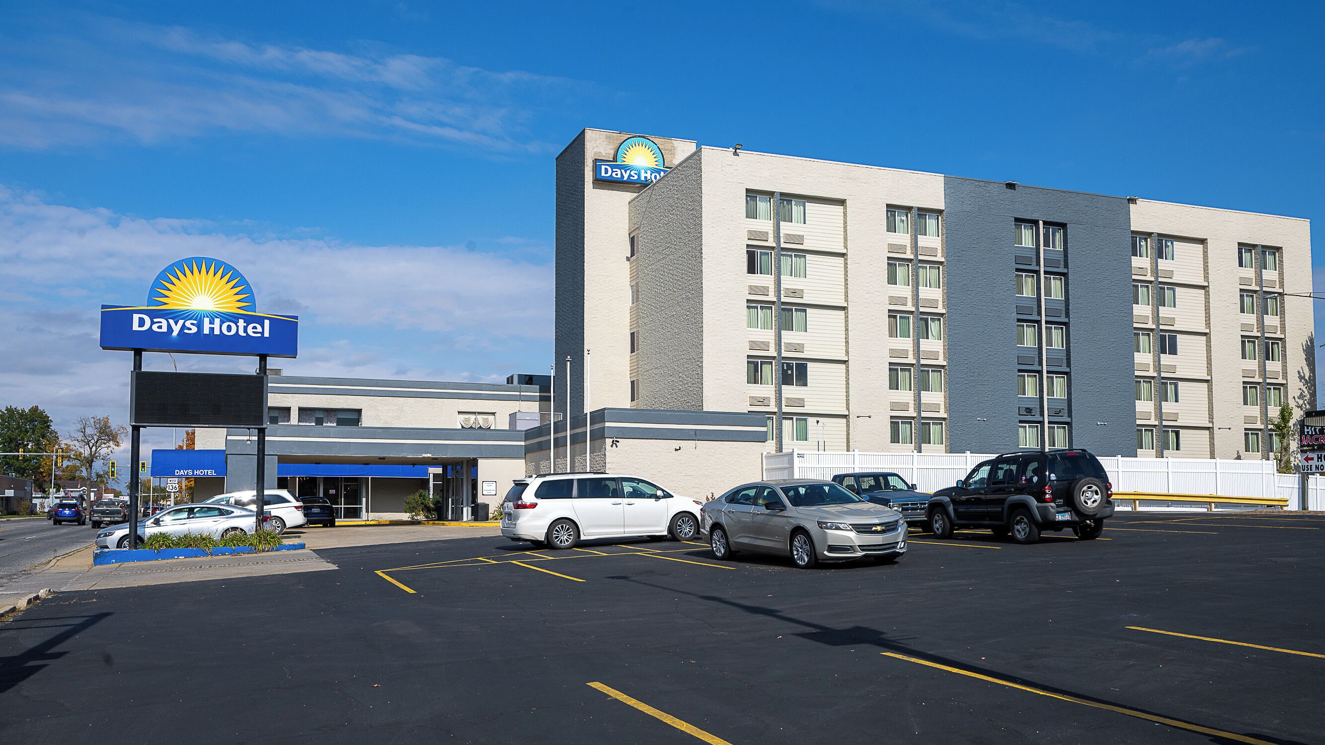 A Days Hotel with a parking lot, a building with multiple floors, and a clear sky.