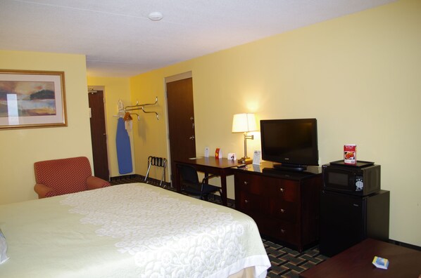 A hotel room with a bed, a desk with a television, a microwave, a chair, and a coat rack.