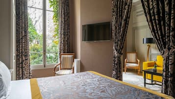A hotel room with a large bed, two chairs, a TV mounted on the wall, and a window with curtains.