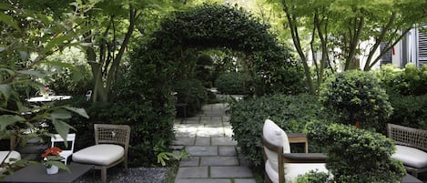 A garden pathway with a stone archway, surrounded by lush greenery and seating areas.